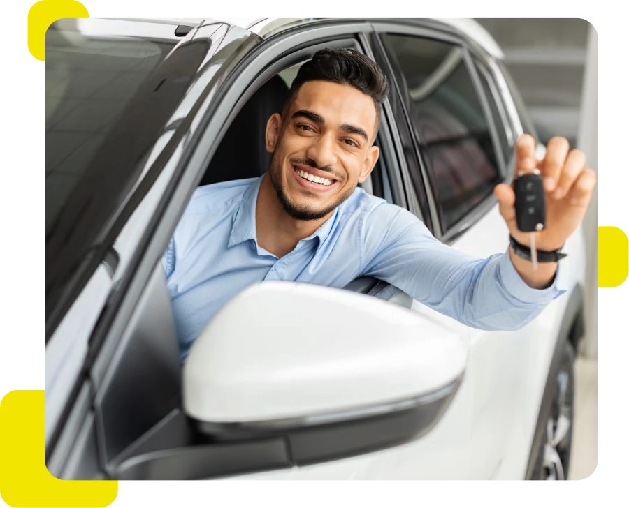 Homem jovem sorrindo e segurando a chave de um carro enquanto está sentado no banco do motorista.
